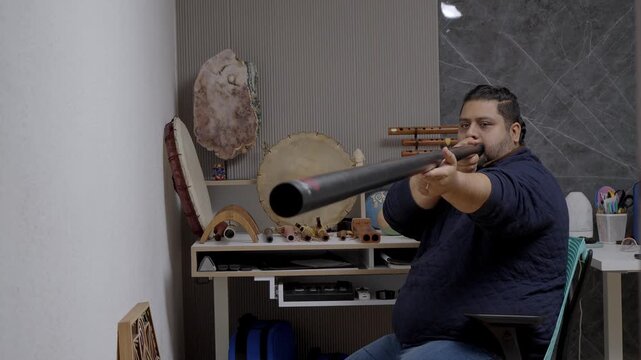Man practicing circular breathing technique while playing a didgeridoo. Ethnic wind instrument and sound healing session in a music studio