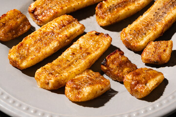 golden-brown baked or fried plantain slices dusted with spices, arranged on a light grey, beaded-rim plate on a green wooden surface