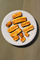 golden-brown baked or fried plantain slices dusted with spices, arranged on a light grey, beaded-rim plate on a green wooden surface