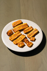 golden-brown baked or fried plantain slices dusted with spices, arranged on a light grey, beaded-rim plate on a green wooden surface
