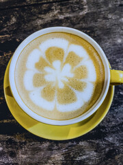 Top-down Hot cappuccino with Beautiful Flower latte art in cafe, served in bright yellow earna porcelain cup and wooden table