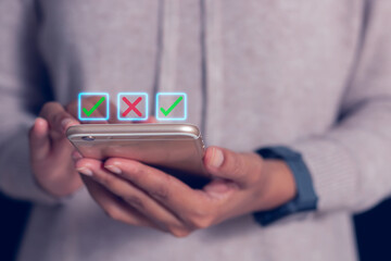 Close-up of hands holding smartphone with glowing check and cross icons, symbolizing digital decision making, online voting and mobile application.