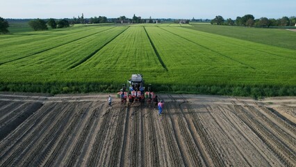 A group of farmers inspect a field of crops with a tractor in the background showcasing agricultural work and rural landscapes