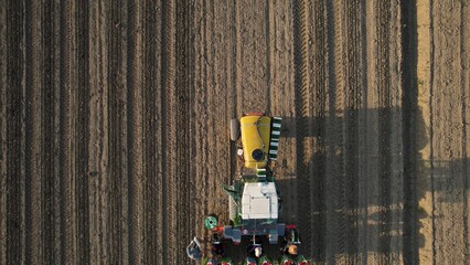 High Angle Aerial View of a Modern Tractor Planting Seeds in a Large Agricultural Field During Sunrise Creating a Beautiful Pattern of Rows