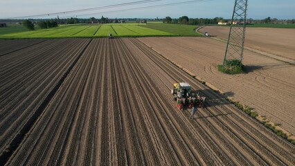 High angle view of a tractor planting seeds in a large agricultural field on a sunny day with a transmission tower in the background