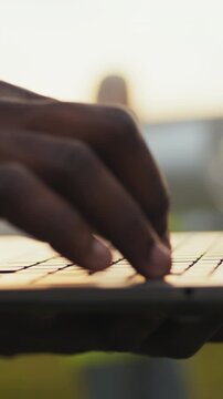 A person's hands typing on a laptop keyboard, with a blurred background of the sunset.