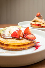 Stacked pancakes topped with fresh fruit, chocolate hazelnut spread, and strawberry sauce