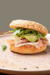 Bagel sandwich showcasing fresh prosciutto, creamy avocado, and vibrant arugula on a sesame seed bun