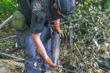 A sapper in protective gear holds an unexploded artillery shell