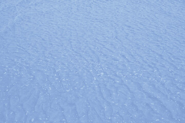 A close-up horizontal shot of a water surface with ripples and bubbles. The color is blue, with a soft, gentle texture and natural light. view from above