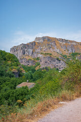 Scenic view of a rugged rocky mountain with ancient cave dwellings and ruins nestled among green trees and dry grass hillsides. A perfect blend of natural beauty, history, and adventure