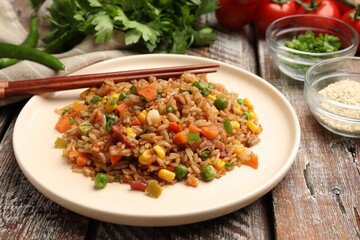 Delicious fried rice with vegetables and bacon served on wooden table, closeup