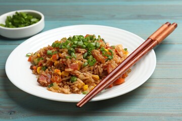 Delicious fried rice with vegetables and bacon served on light blue wooden table, closeup