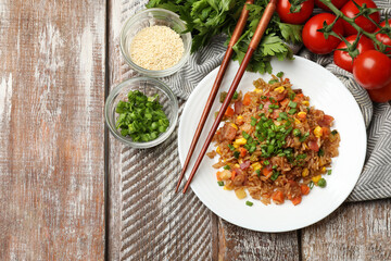 Delicious fried rice with vegetables and bacon served on wooden table, flat lay. Space for text