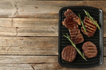 Delicious grilled beef meat with rosemary on wooden table, top view. Space for text