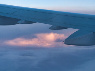 Fototapeta premium An aerial view from an airplane window, showcasing the wing and engine against a dramatic, cloudy sky with soft pink and blue hues.