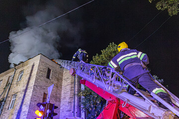 Firefighters extinguishing a burning building at night using a ladder truck © Vladyslav 