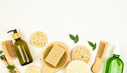 Natural soap bar with wooden brushes, combs, green glass pump bottles, and loofah sponges arranged on white background, evoking fresh and eco friendly skincare routine