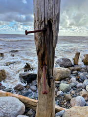 Weathered groyne post with rusty bolts by sea waves, rustic maritime coastal structure.