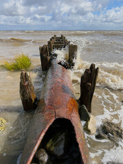 Rusty outfall pipe leading into sea with waves crashing, dramatic maritime coastal scene.
