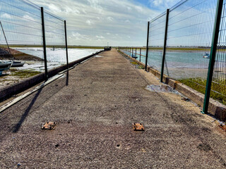 Concrete pier with metal fences extending into estuary waters, dramatic coastal industrial scene.