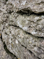 Close up of rough weathered stone wall texture with cracks and rugged detail, ideal for natural backgrounds.