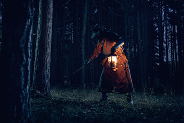 Mysterious figure illuminated by lantern navigates dark, dense forest.