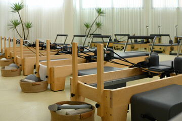A Pilates studio featuring a row of wooden reformers with accessories, perfectly aligned for group training in a bright, serene space