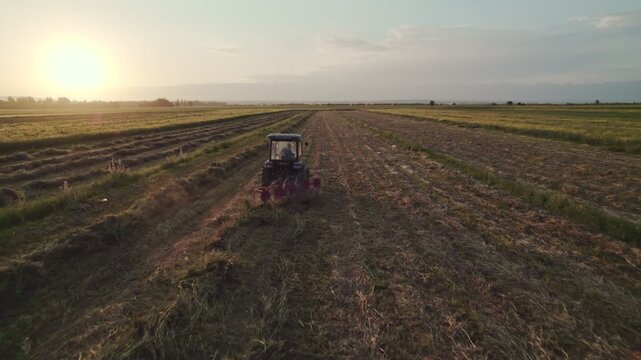 Tractors With Hay Rake And Baler Working In Field At Golden Hour Epic Aerial CInematic. Tedder for tractor. The machine for gathering hay.