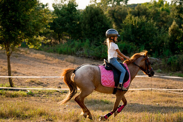 young girl horseback riding on a horse sunset in the countryside smiling in a ranch. sport and hobby