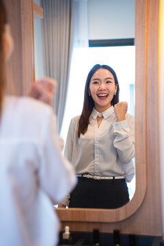 Young adult female asia people self love cheer up pep talk before start working. girl standing look in front of mirror smile at home in mental health care or work career stress relief.