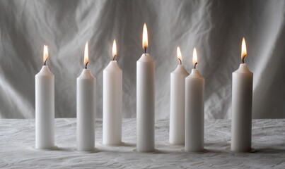Five or six white candles stand upright, lit and glowing softly. Their flames flicker gently, casting a warm light, creating a calm atmosphere suitable for relaxation or meditation
