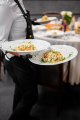 Waiter serving plated rice and vegetable dishes at a formal event. Professional service, elegant table setting, and catering atmosphere captured in motion