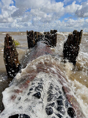 Rusty outfall pipe with sea waves splashing and water droplets mid air, dramatic maritime coastal scene.