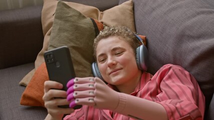 Top view shot of smiling young woman with prosthetic hand holding smartphone above while watching videos relaxing on couch - Powered by Adobe