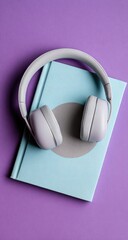 Light gray headphones resting on a light blue notebook, top view on a vibrant purple background