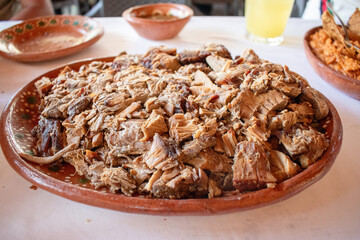 Authentic birria dish on a rustic clay plate accompanied by rice, salsa and a beverage