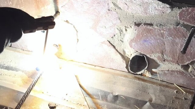 Welding work using electrodes. Welding two bars of reinforcement to create a frame for stairs in the country. Repair and construction work close-up. A person welds metal parts. Flash from welding work