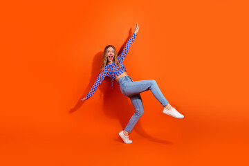 Cheerful young woman with blonde hair posing playfully against a vibrant orange background, wearing a stylish casual outfit