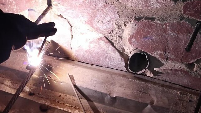 Welding work using electrodes. Welding two bars of reinforcement to create a frame for stairs in the country. Repair and construction work close-up. A person welds metal parts. Flash from welding work