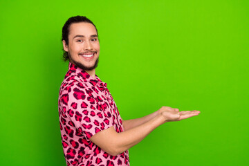 Confident young man in a stylish pink leopard print shirt smiling and gesturing with open hands against green background