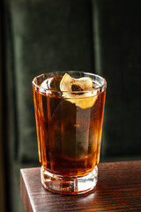 Whiskey cocktail with ice and dried fruit garnish in crystal glass on dark background, close up
