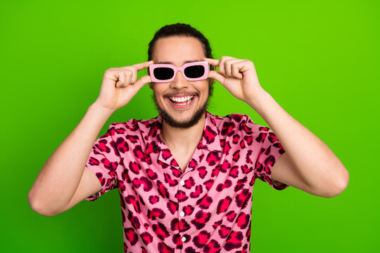 Happy young man in stylish pink leopard print shirt and sunglass posing on green background, enjoying holidays - Powered by Adobe