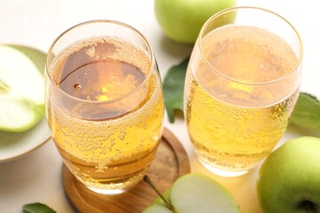 Fresh cider in glasses, apples and green leaves on beige table, closeup