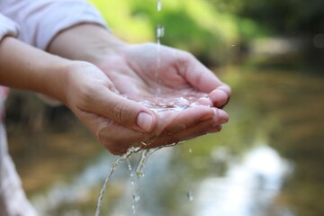 Save water concept. Woman holding her hands under flowing clean water near river outdoors, closeup
