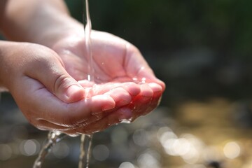 Save water concept. Little girl holding her hands under flowing clean water near river outdoors, closeup. Space for text
