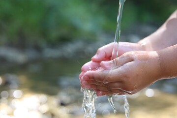 Save water concept. Little girl holding her hands under flowing clean water near river outdoors, closeup. Space for text