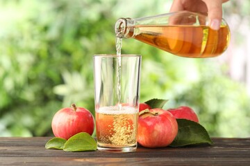 Woman pouring delicious cider into glass at wooden table outdoors, closeup