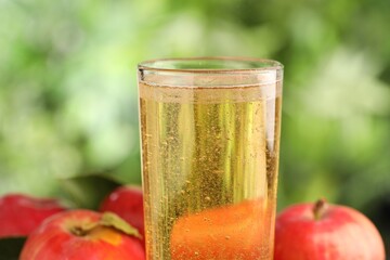 Delicious cider in glass and apples on blurred background, closeup