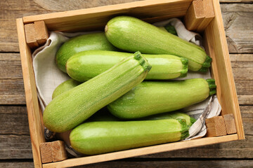 Fresh ripe zucchinis in crate on wooden table, top view